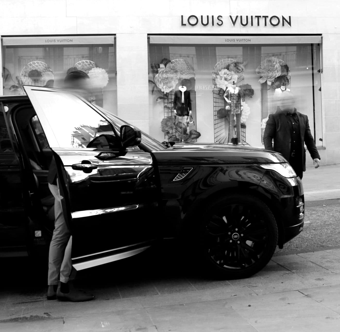 A black BPS Range Rover at the kerb outside a boutique, an officer standing by the rear door